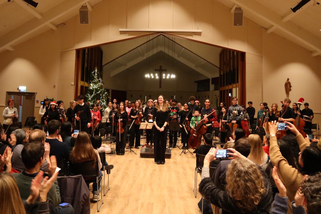 Image shows the orchestra standing to applause from the audience