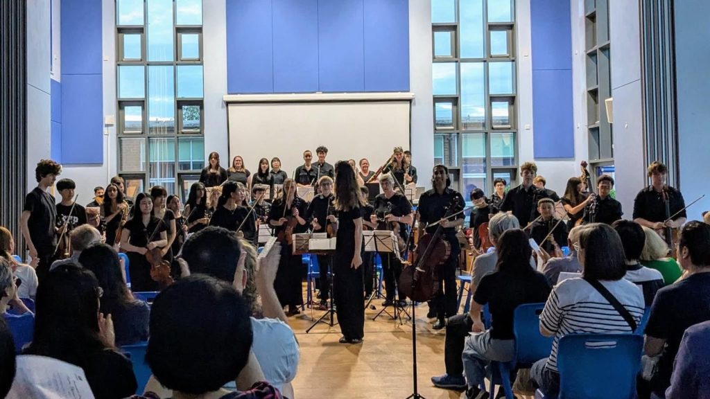 An orchestra in a hall standing up to receive applause from the audience